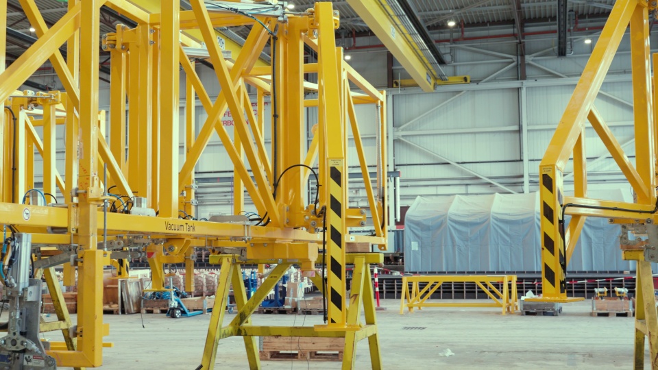 Still from the HAWART film: yellow steel assembly frames in the production hall