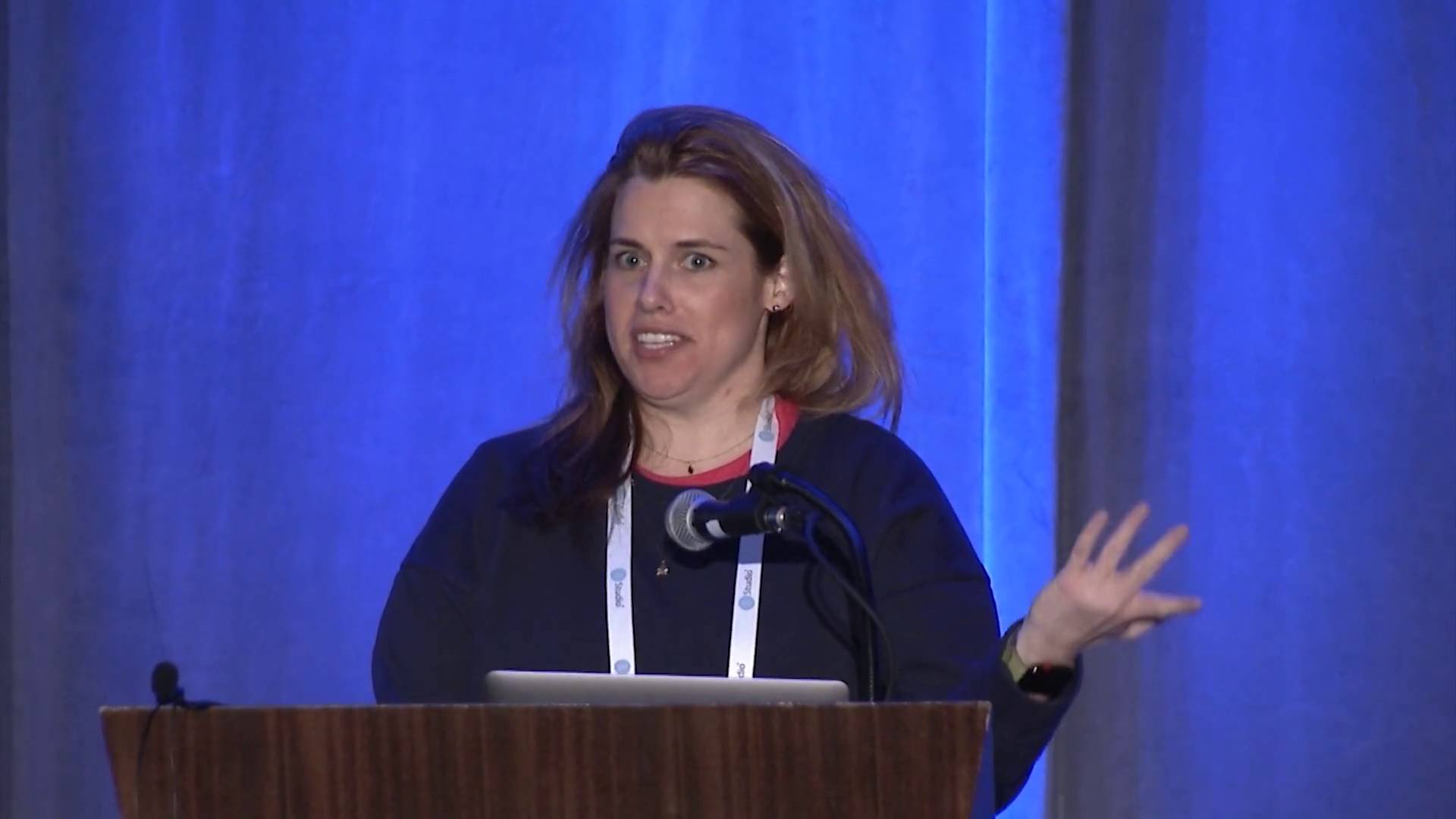 Picture of woman standing behind podium giving a talk. Thumbnail from video.