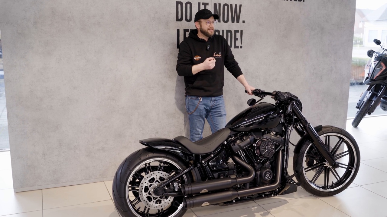 Still from the dealership film: a man standing next to a black Harley-Davidson motorcycle