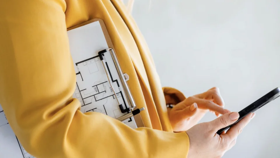 woman with floor plans on clipboard tucked under her arm while checking her phone